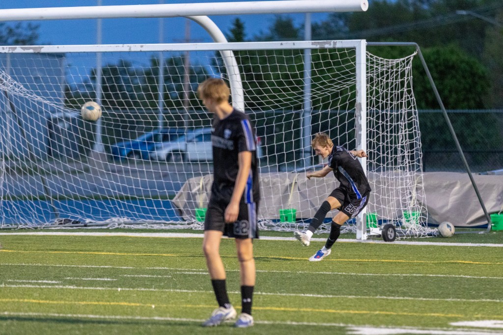 A soccer player kicks the ball towards the goal while another player watches on the field during a game.