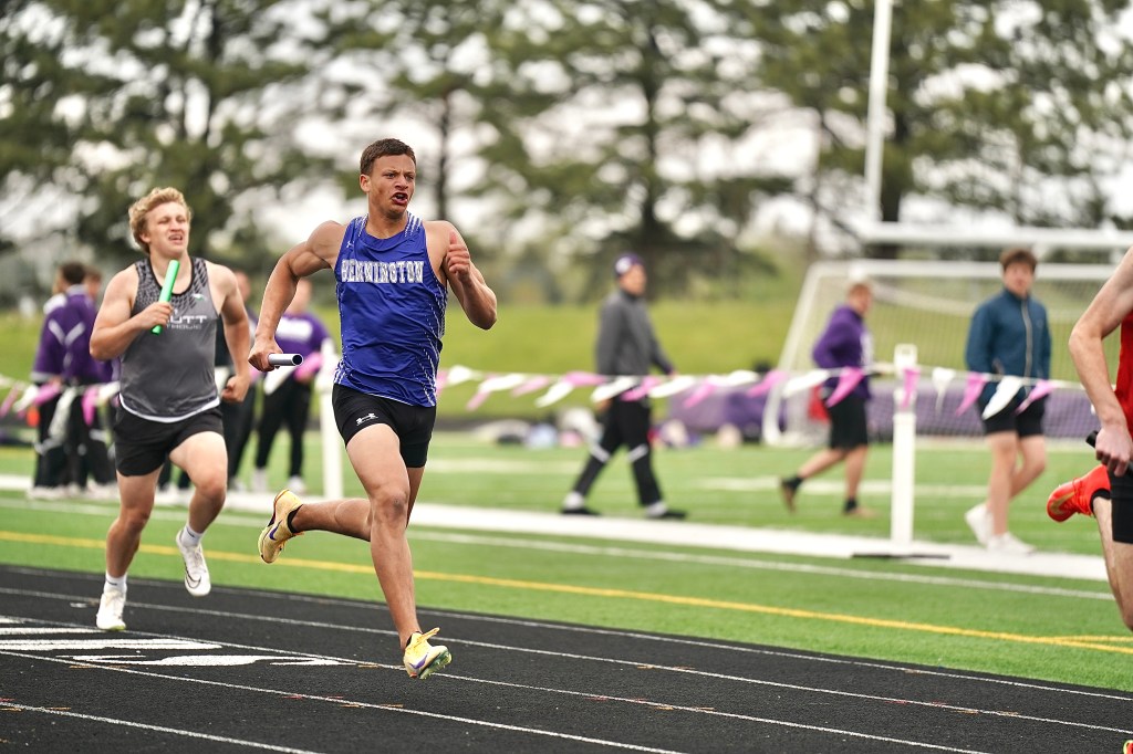 Two male track athletes sprinting in a relay race on a track, one holding a baton while the other is close behind.