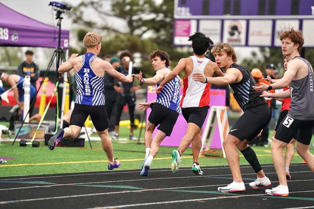 Athletes participating in a relay race, passing the baton on a track field during a competitive event.
