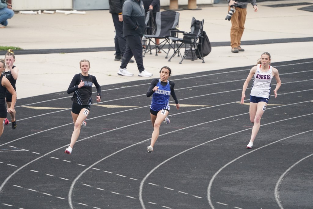 Four female athletes competing in a sprint race on a track, showing intense focus and determination.