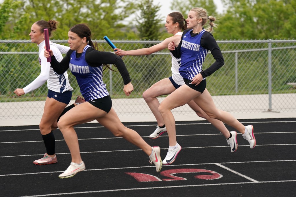 Four female runners in a relay race, passing batons on a track.