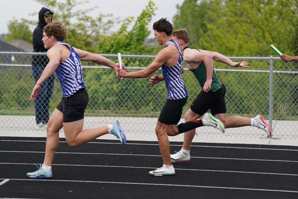 Three track athletes in a relay race, with one athlete passing a baton to another on a running track.
