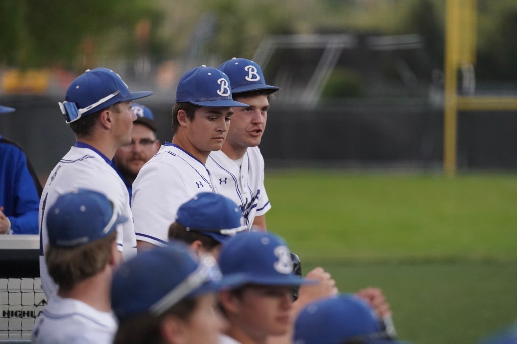 A group of baseball players wearing blue hats and white jerseys sit on the bench, focusing on the game.