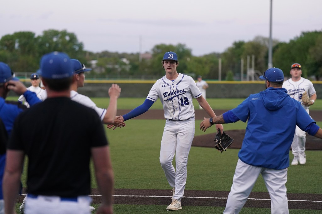 A baseball player in a white uniform with the number 12 shakes hands with teammates on the field, showcasing a moment of camaraderie during a game.