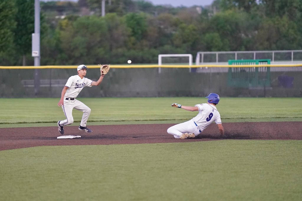 A baseball player attempts to catch a ball while another player slides into second base during a game.