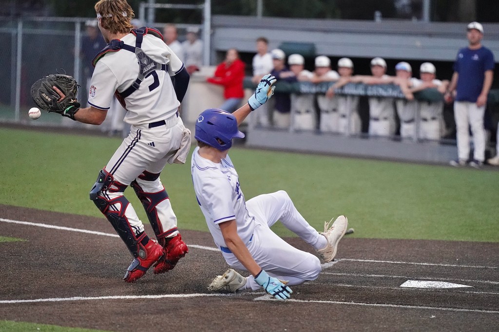 A baseball player sliding into home plate as the catcher attempts to catch a thrown ball.