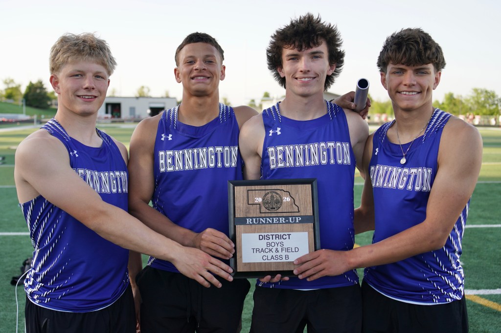 Four high school track and field athletes in blue jerseys holding a runner-up plaque for district boys track and field competition.