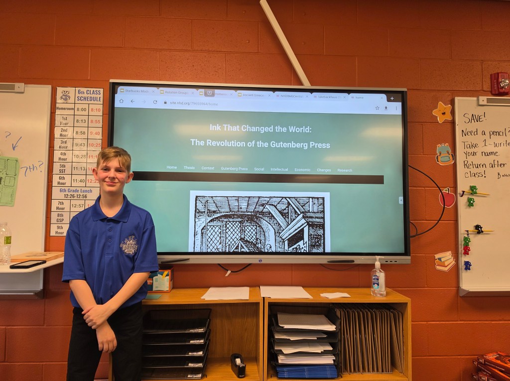 A student stands in front of a large screen displaying a website titled 'Ink That Changed the World: The Revolution of the Gutenberg Press.' The classroom features a class schedule to the left and various classroom items on a shelf below the screen.