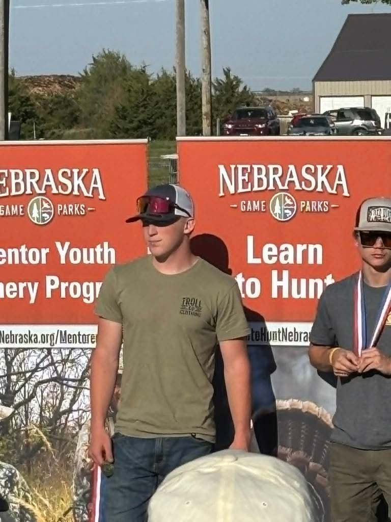 Two young men standing in front of Nebraska Game Parks banners, promoting youth mentorship and hunting programs.