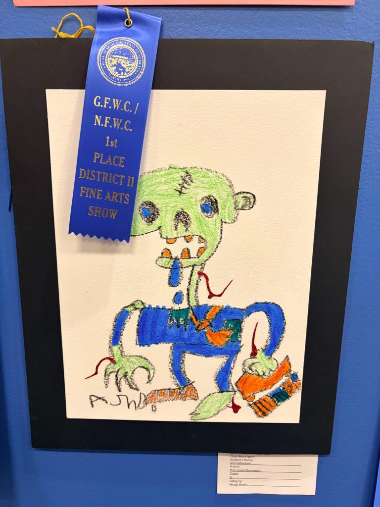 A colorful children's drawing of a cartoon zombie with a green head, blue shirt, and orange pants, displayed with a blue ribbon indicating 1st place in a fine arts show.
