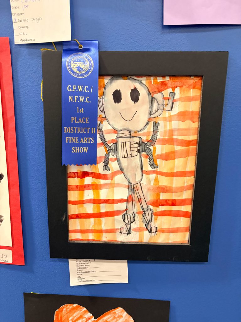Drawing of a robot with a smiling face, framed and displayed with a blue ribbon indicating 1st place in a fine arts show.