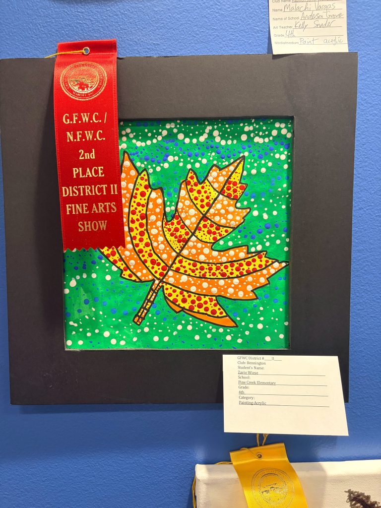 An artwork featuring a colorful painted leaf on a green and blue background, displayed in a black frame. A red ribbon indicates it won 2nd place in a fine arts show.