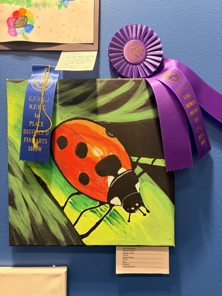 A colorful painting of a ladybug on green leaves, displayed with a blue first place ribbon and a purple award ribbon on a wall.