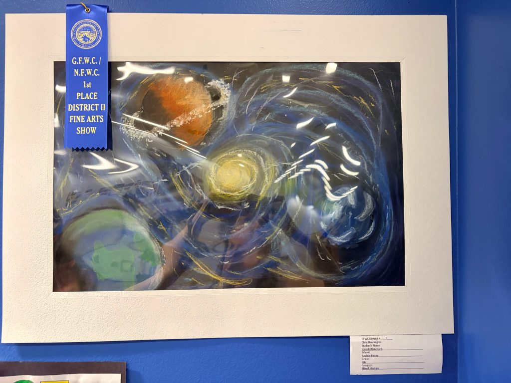A colorful painting depicting a cosmic scene with planets and swirling stars, framed in white, accompanied by a blue ribbon indicating 1st place in a fine arts show.