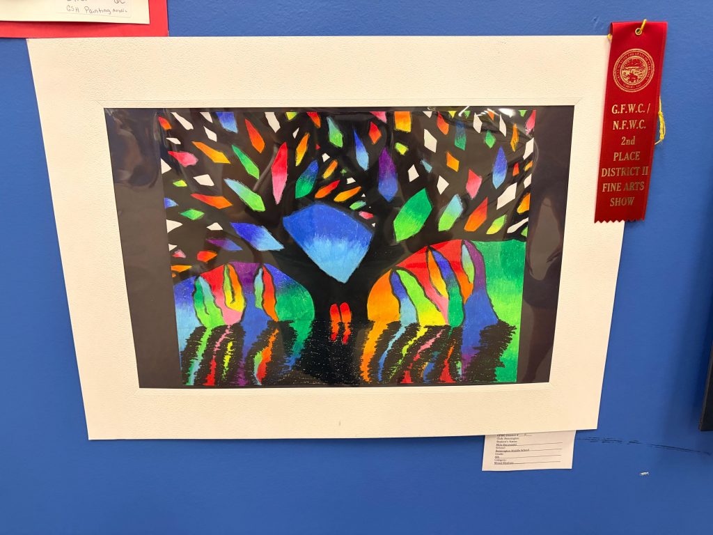 A vibrant artwork depicting a tree with colorful leaves against a bright background, framed and displayed on a blue wall. A red ribbon indicating 2nd place in a district fine arts show is attached to the display.