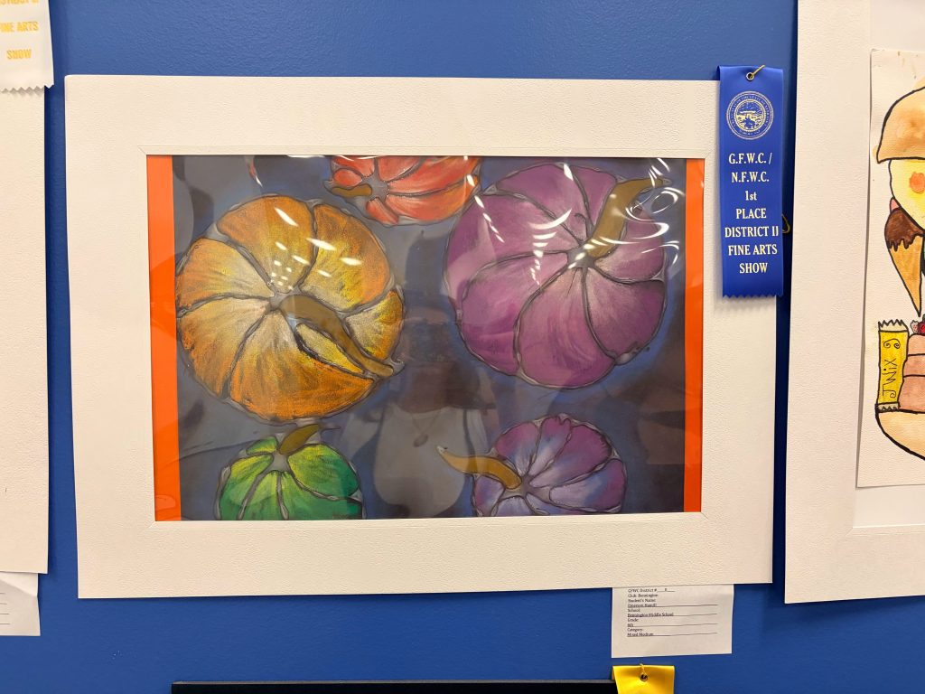 A framed artwork featuring colorful pumpkins in various shades, with an orange matting and a blue ribbon indicating a first place award at a fine arts show.