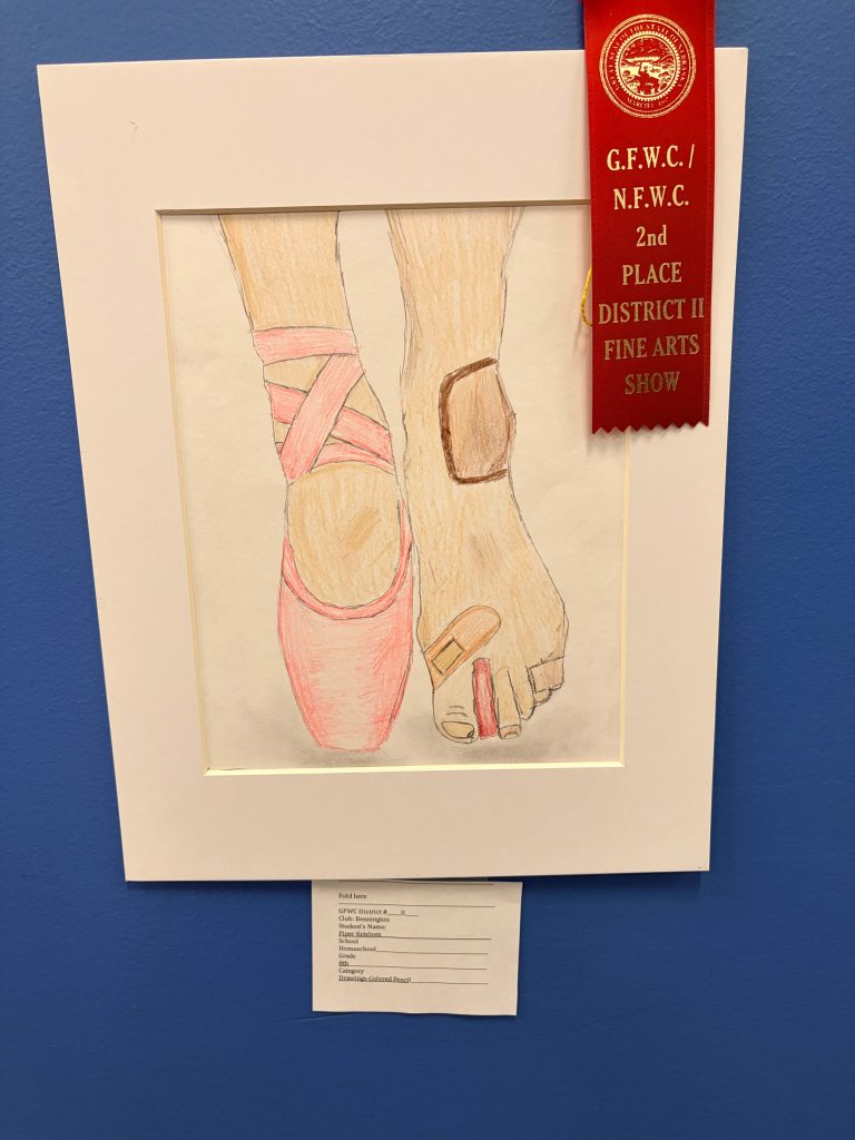 A framed colored drawing displaying two feet; one bare foot with a bandage and the other wearing a pink ballet shoe. A red ribbon indicating a second place award is attached to the top of the frame.