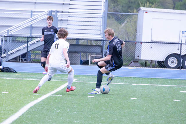 Two soccer players on a field, one wearing a black jersey and the other in white, competing for the ball.