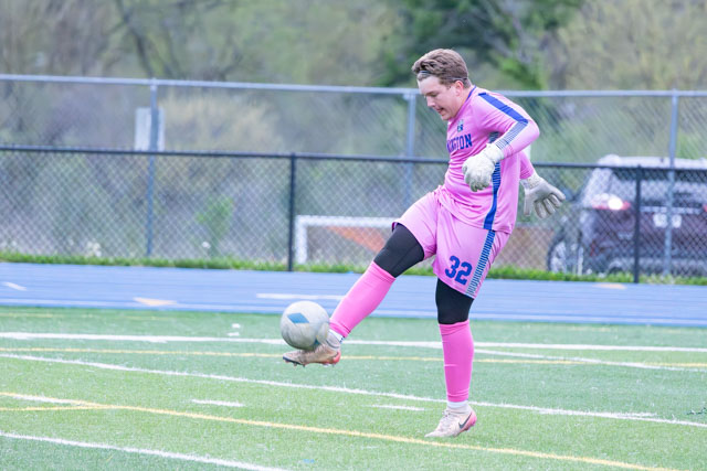 A soccer goalkeeper wearing a pink uniform is preparing to kick a soccer ball on a grassy field.