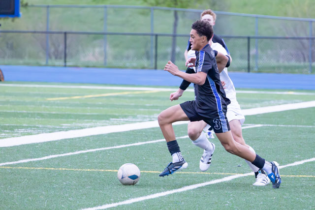 Two young male soccer players competing for possession of a soccer ball on a turf field.