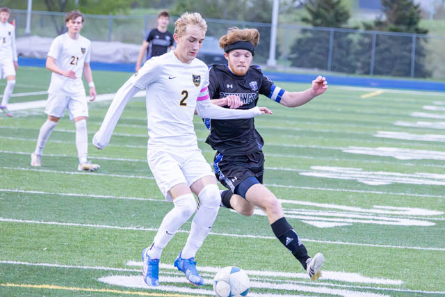 Two soccer players in action on a field, one in a white jersey and the other in black, competing for the ball.