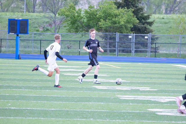 A soccer game in progress, featuring two players competing for the ball on a green field marked with white lines. One player is wearing a black uniform while the other is in white.