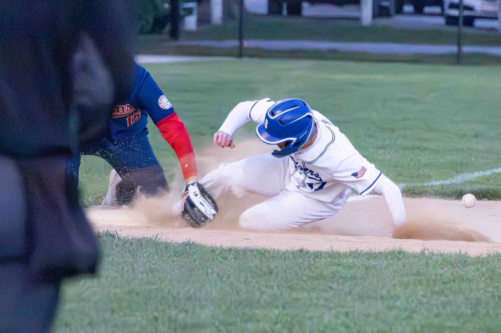 A baseball player slides into home plate, kicking up dust as a catcher prepares to tag him out.
