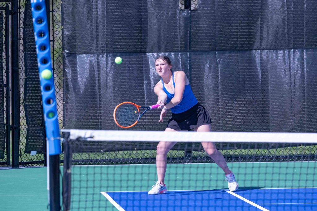 A female tennis player hitting a ball during a match, wearing a blue top and black shorts on a tennis court.
