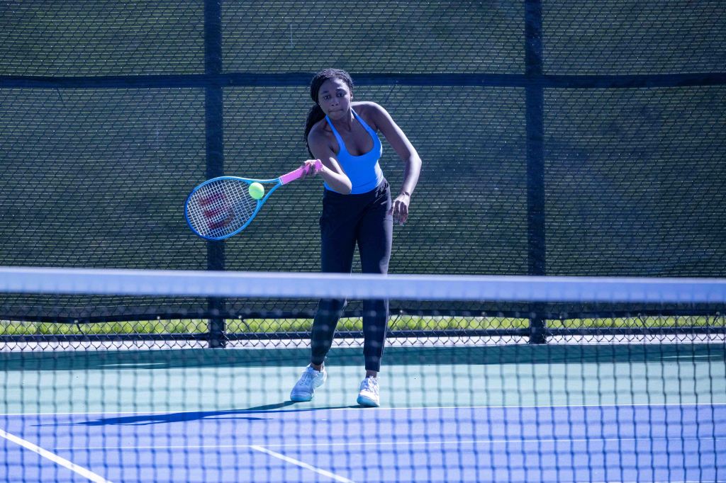 A female tennis player in action, preparing to hit a tennis ball with a racket on a court surrounded by a net.