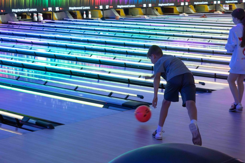 A young child bowling in a colorful bowling alley, with neon lights illuminating the lanes.
