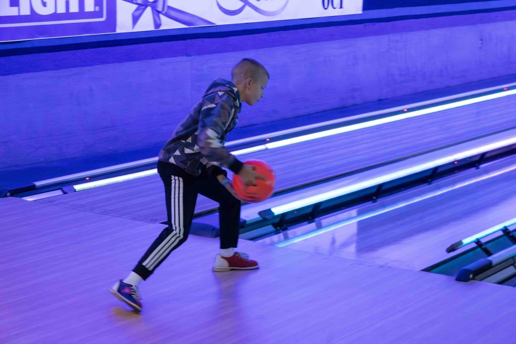 A young child preparing to roll a bowling ball down a lane in a dimly lit bowling alley with purple lighting.