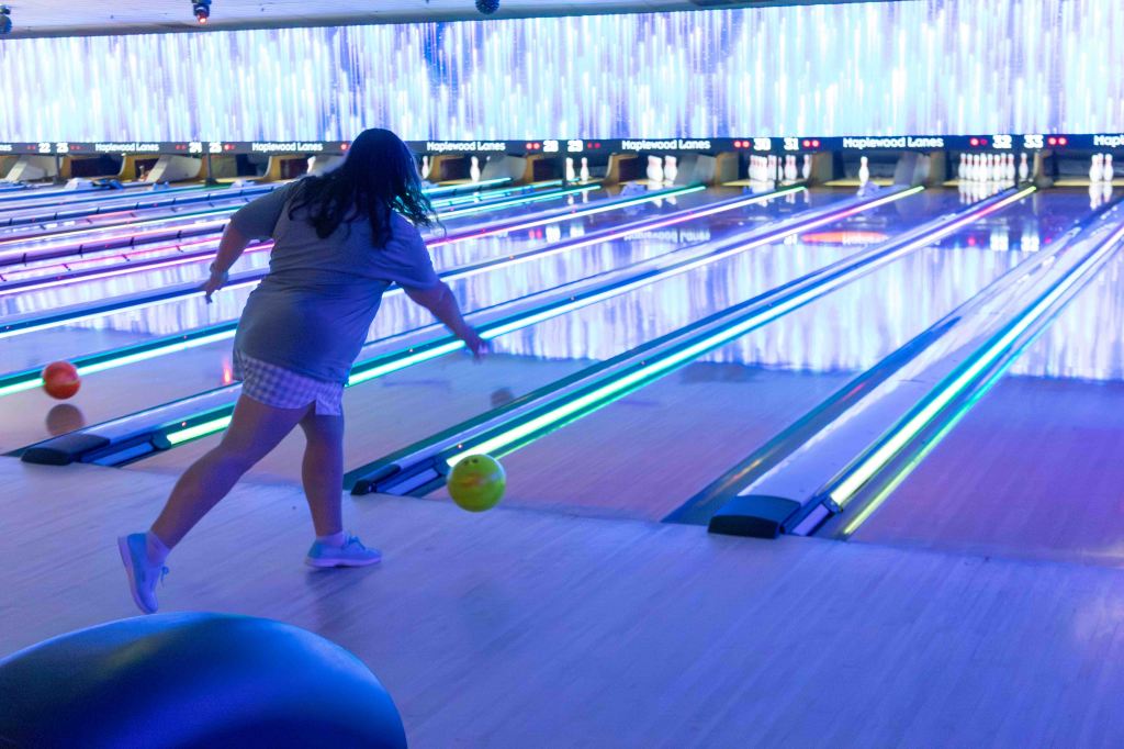 A person bowling in a brightly lit bowling alley with neon lights, focusing on rolling a bowling ball down the lane.
