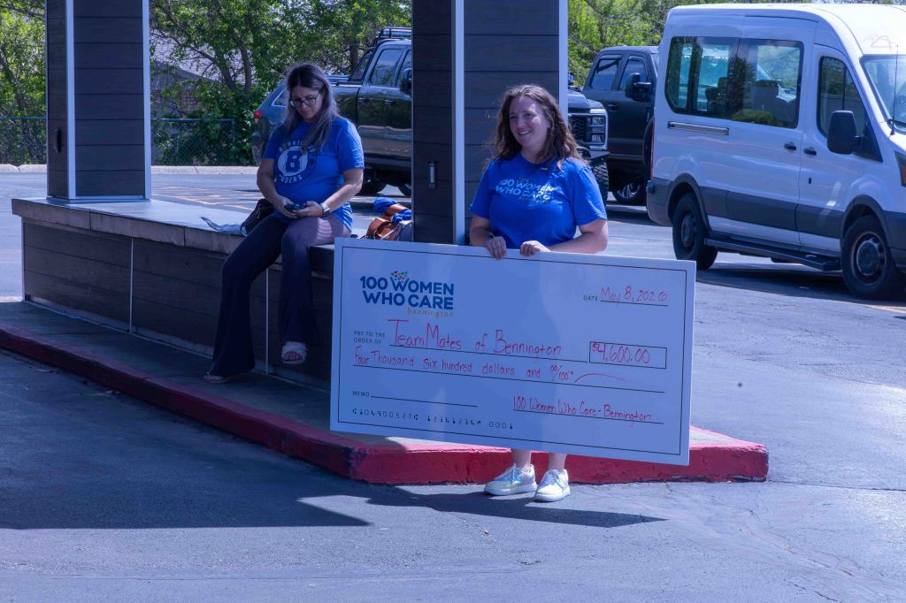 A woman holding a large check for $4,600 made out to 'Team Matters of Bennington' on May 8, 2020, with another woman seated in the background.