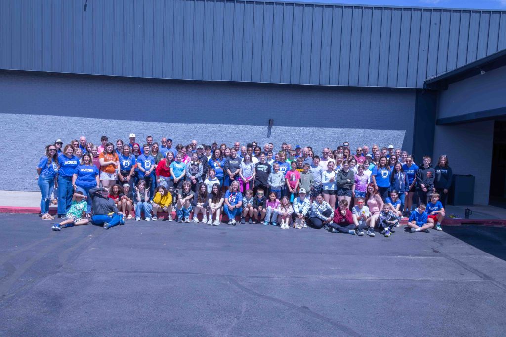 A large group of people of various ages posing together outside a building, smiling at the camera.