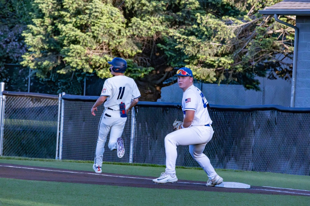 A baseball game scene featuring two players; one is running towards second base while the other is positioned at first base, ready to receive the ball.