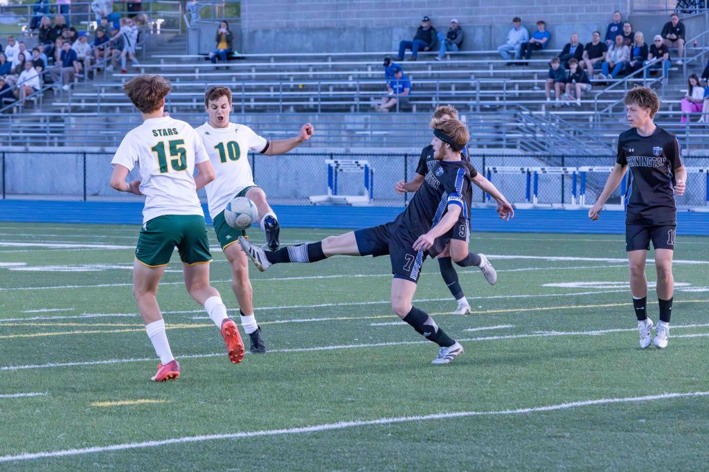 A soccer match in progress, featuring players in white and black jerseys competing for the ball on a green field.