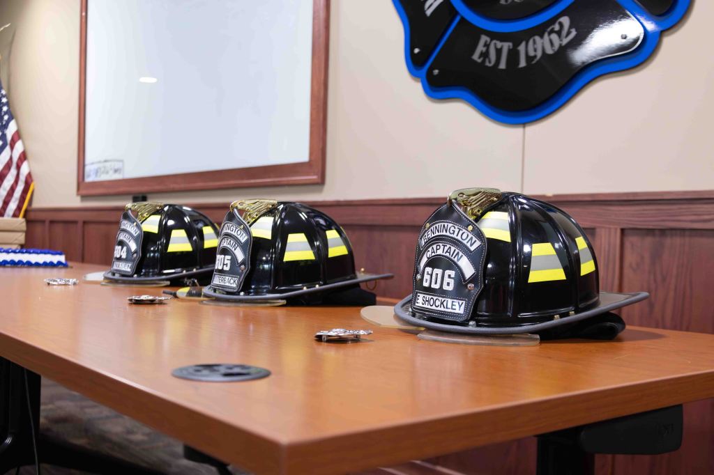 Three firefighter helmets on a wooden table, with badges and an American flag in the background.