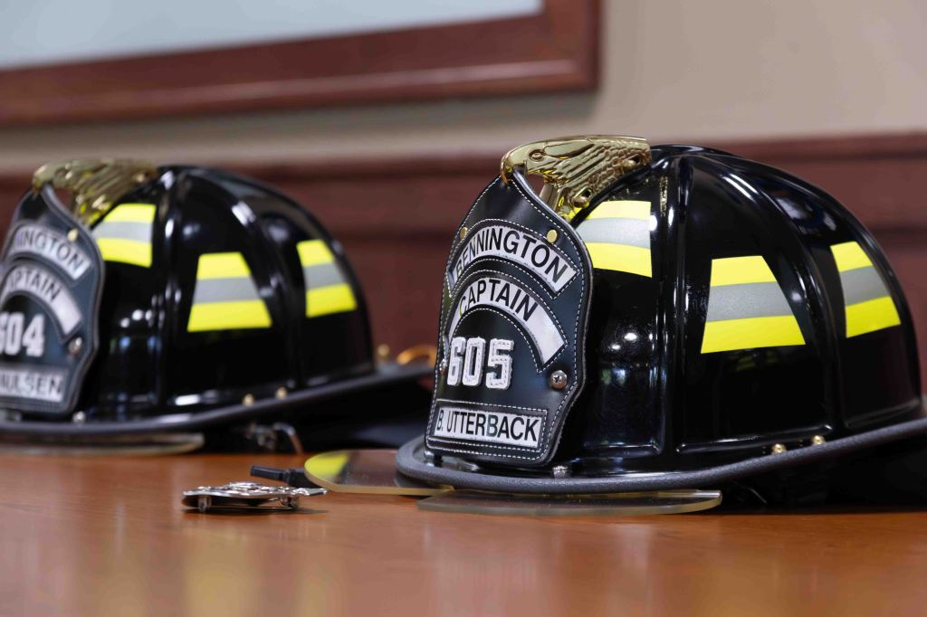 Two black firefighter helmets with reflective yellow stripes on a wooden table, one labeled 'Captain 504' and the other 'Captain 605'.