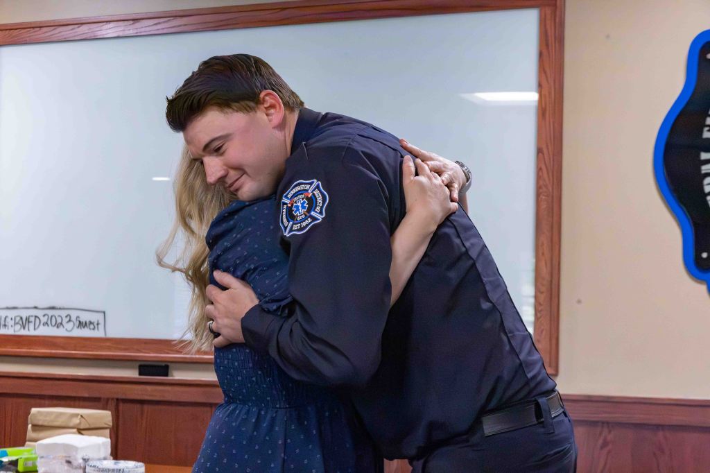 A firefighter and a woman embrace in a supportive hug, showcasing an emotional moment in a classroom setting.