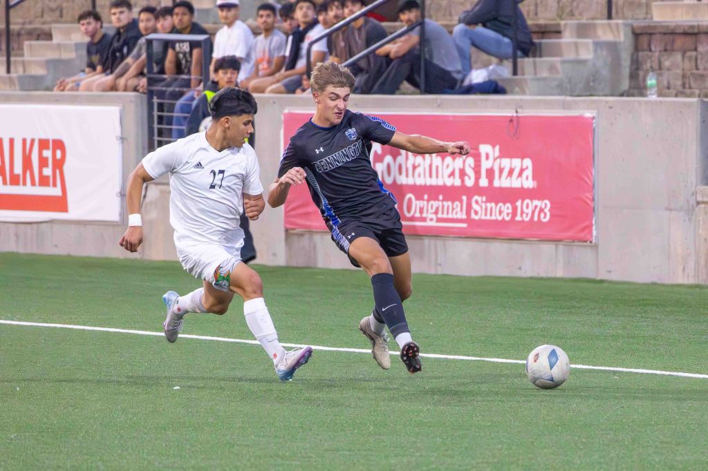 A soccer match in progress, featuring two players competing for the ball. One player in a white uniform, number 27, is sprinting towards the ball, while the other player in a black uniform is reaching for it. The backdrop includes spectators in a stadium setting.
