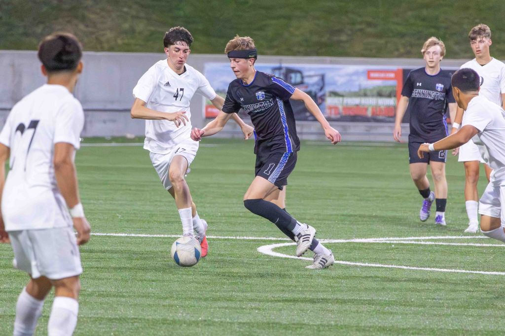 A youth soccer match in progress, featuring players in white and black jerseys competing for the ball on a green turf field.