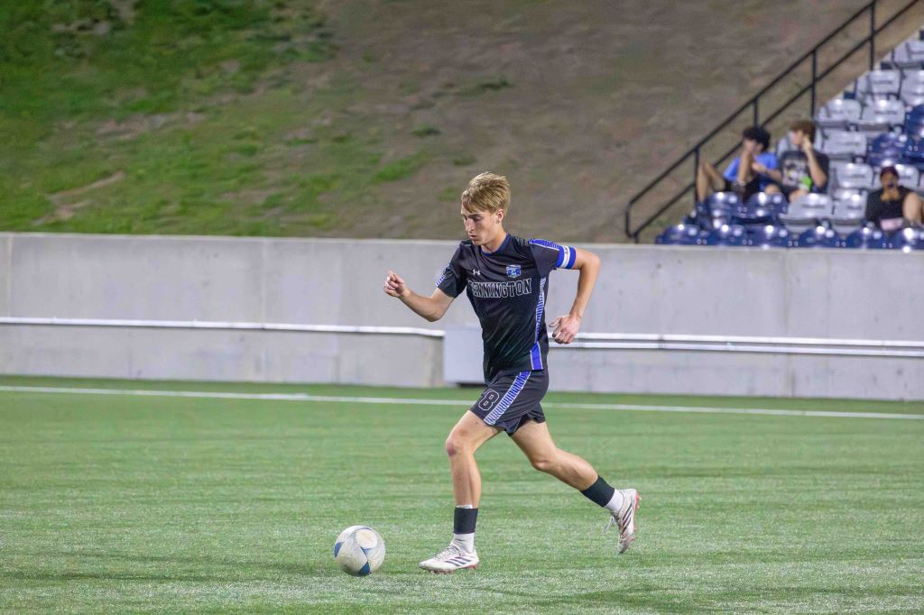 A young male soccer player dribbles a ball on a well-maintained grass field during a night practice.