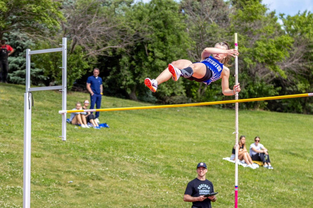 A female pole vaulter in mid-air clearing a yellow bar, surrounded by spectators enjoying the event in a grassy field.