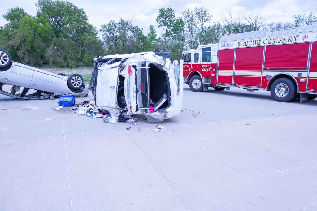 A scene of a vehicle accident featuring a overturned car alongside a rescue truck, with debris scattered on the ground.