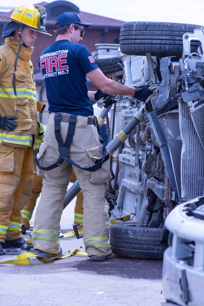 Firefighters assisting at the scene of a vehicle accident with an overturned car.