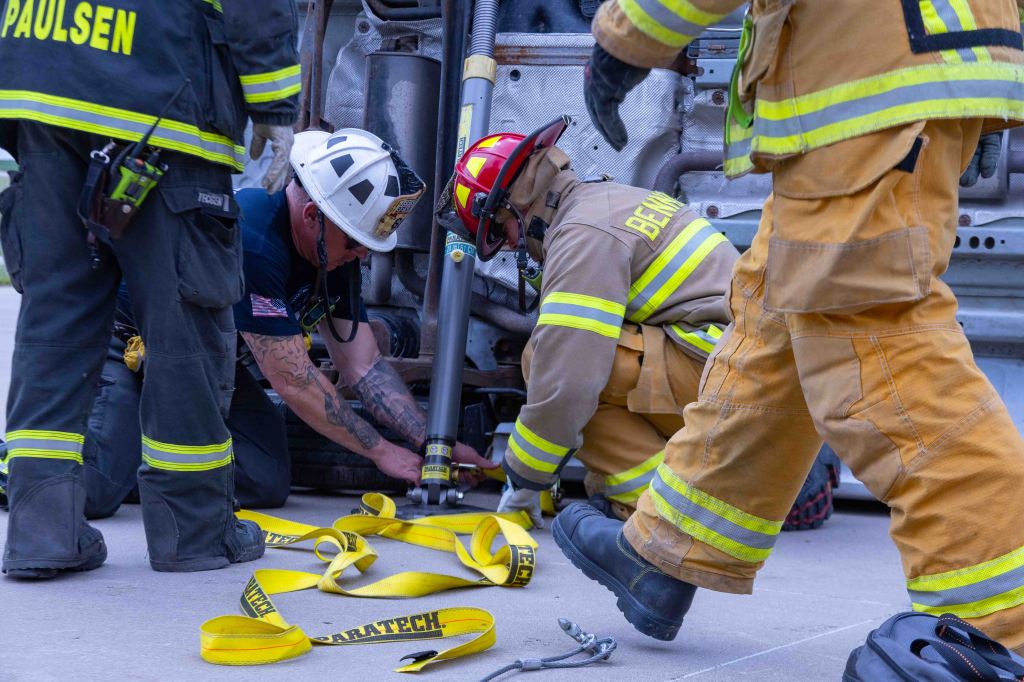 Firefighters working together on a rescue operation, using tools and equipment near a vehicle in distress.