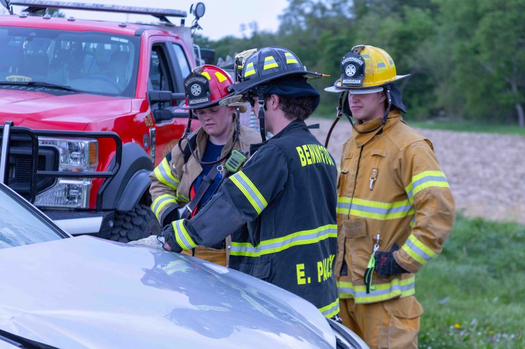 Three emergency responders in uniforms assisting at the scene of an accident near a red fire truck.