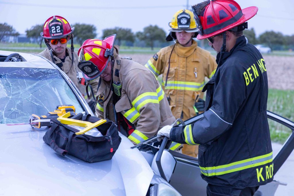 Firefighters working to rescue an injured person from a car with a shattered windshield using rescue tools.
