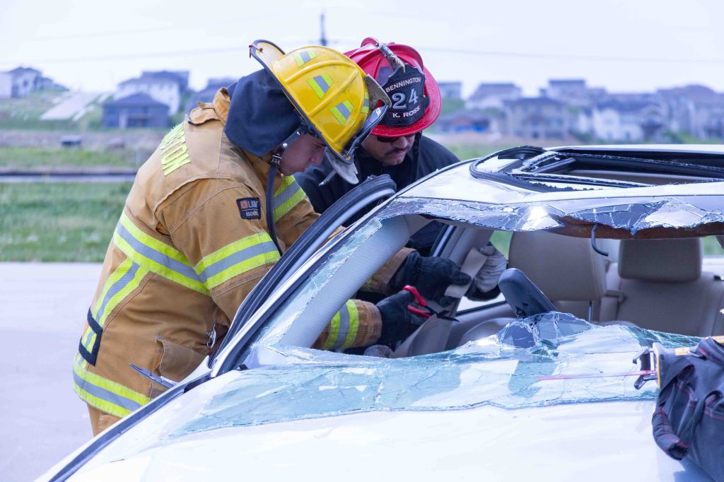 Firefighters working to rescue individuals from a car with a damaged roof during an emergency response.