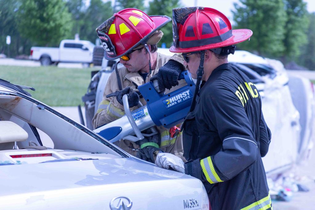 Two firefighters using hydraulic rescue tools to extract a person from a car during a training exercise.